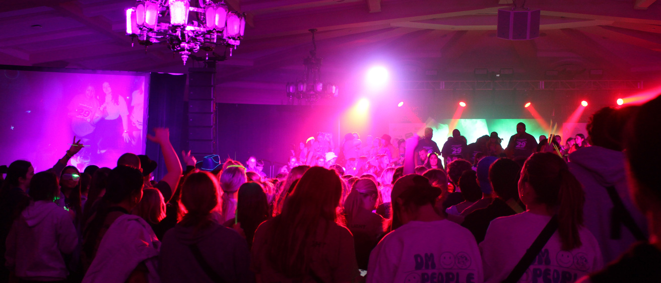 Dark outlines of dancers in the crowd with bright, colored lights shining out from the stage